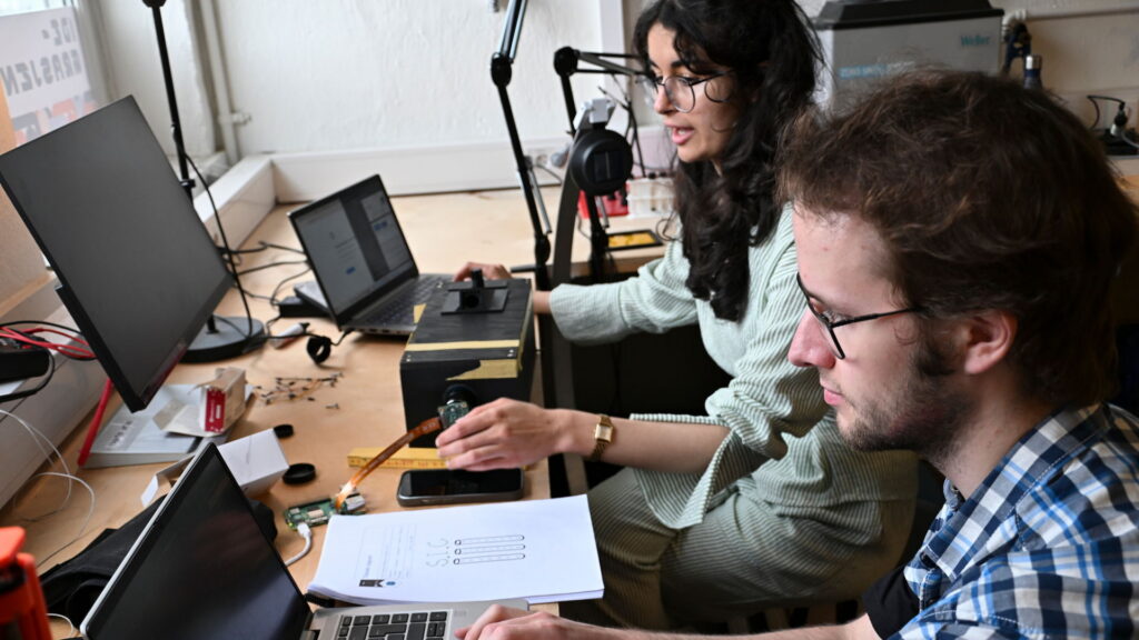 to personer ved hver sin laptop, med firkantet boks mellom seg. foto
