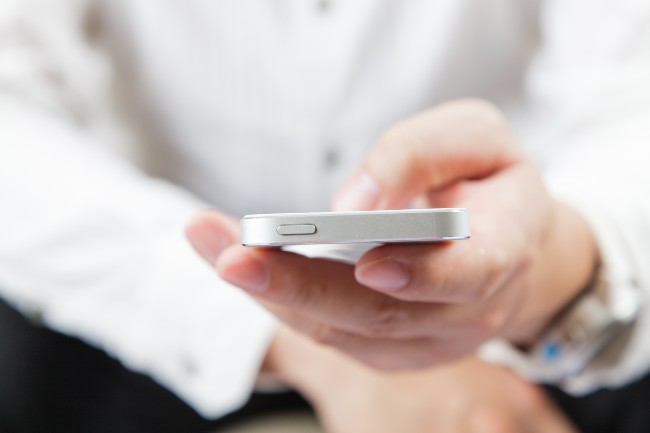 Nærbilde av en hånd som holder en hvit smarttelefon.Foto