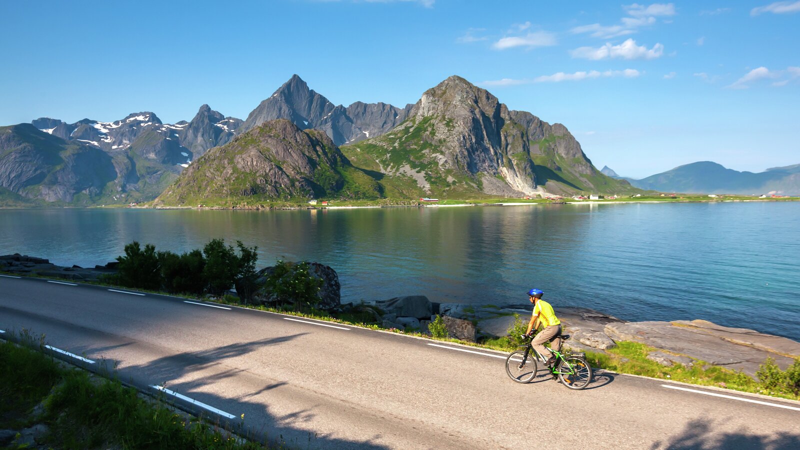 A cyclist cycling in Lofoten with mountains and water in the background