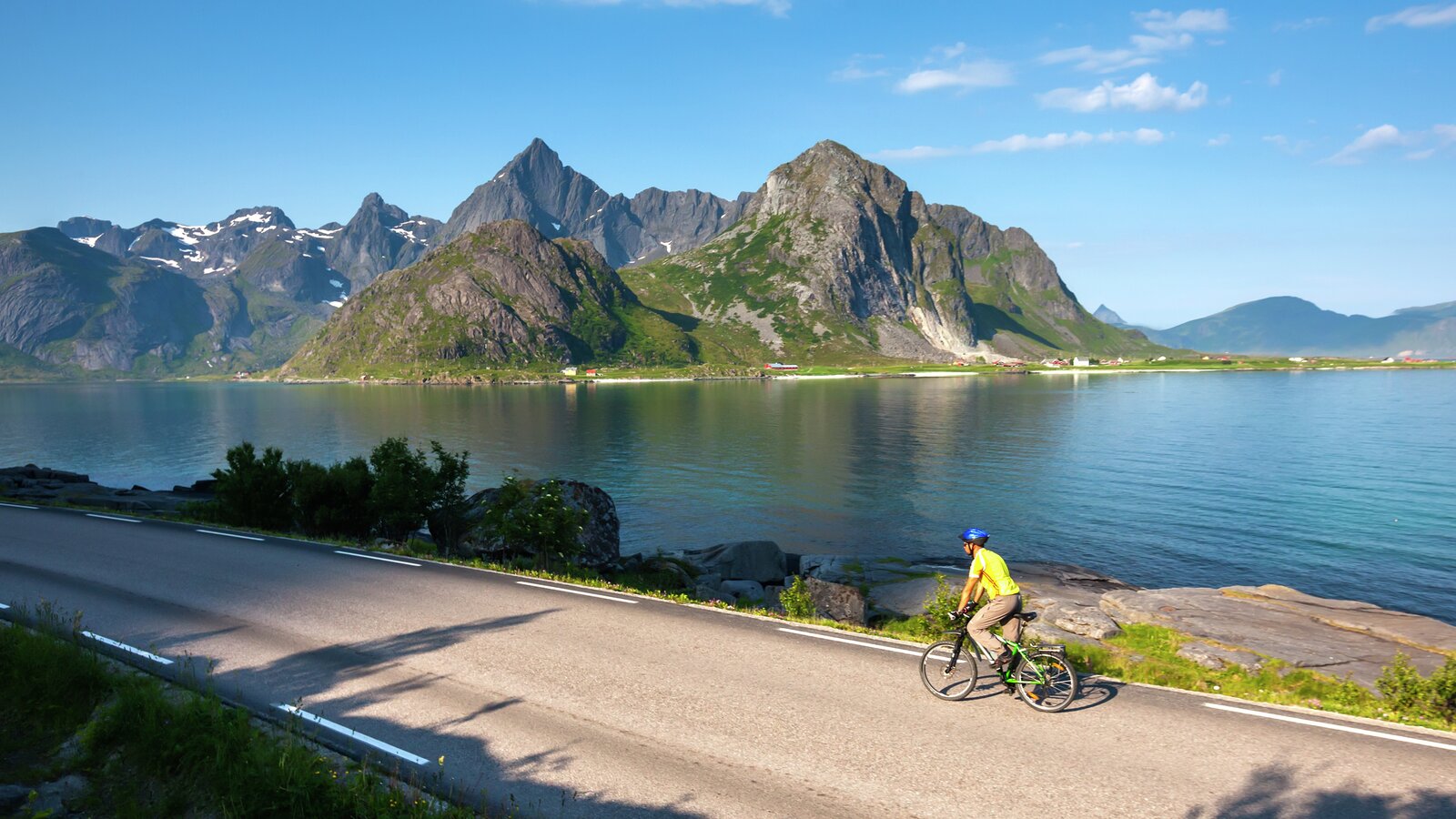 Sylist som sykler i lofoten med fjell og vann i bakgrunn