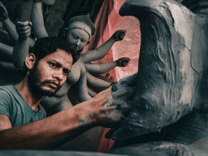 Craftsman shaping a large clay statue of a multi-armed deity in a workshop. — Durga Devi Wallpaper