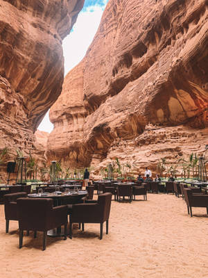 Luxury outdoor dining tables under a red sandstone canyon at sunset. — Saudi Wallpaper