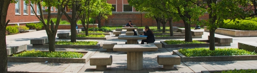 Two students sitting outdoors on a sunny day at different concrete tables on the Purdue campus