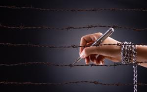 hand with a chain wrapped around the wrist and holding a pen, writing on barbed wire