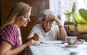 Aged lady being helped with her documents by a young carer, social worker