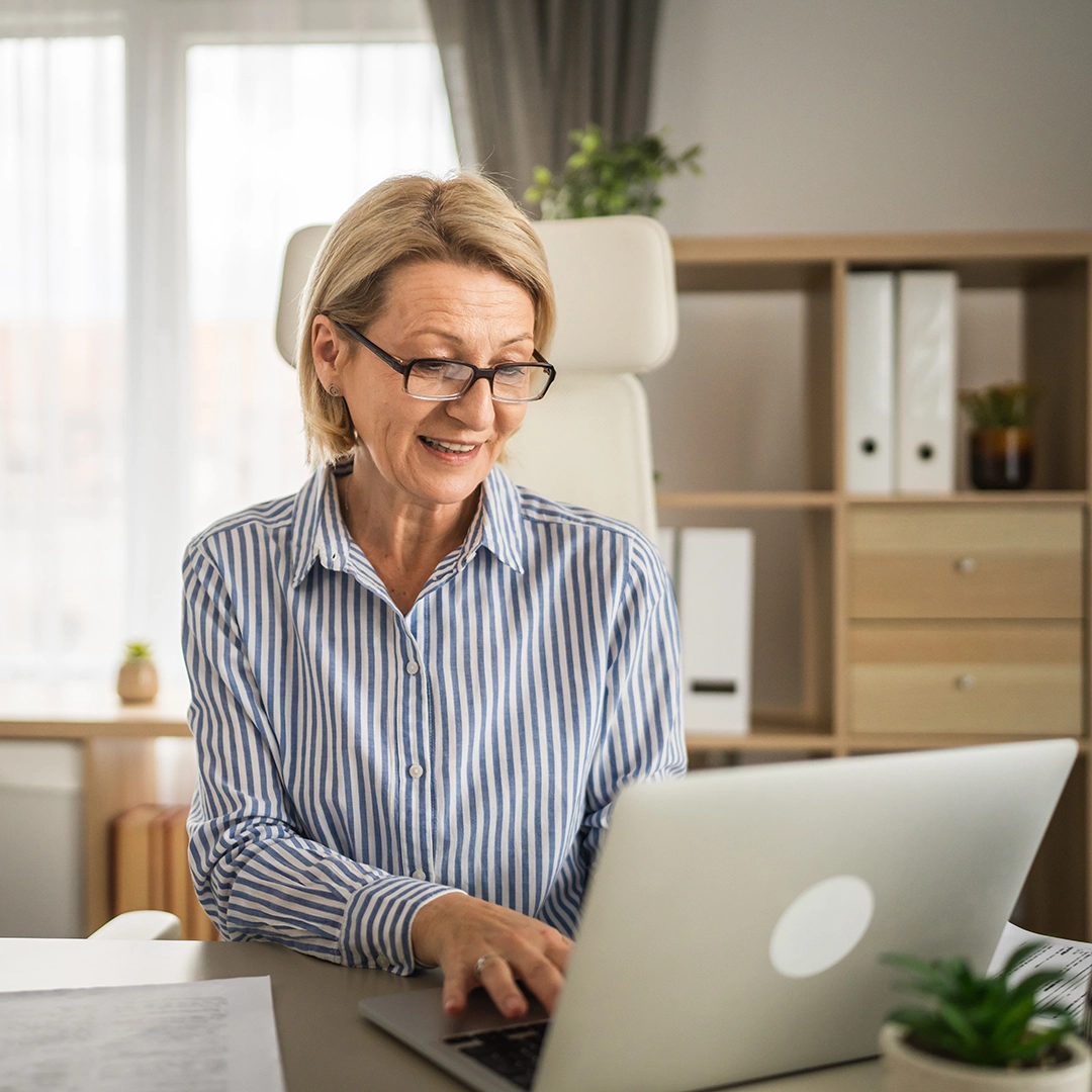 Blid middelaldrende dame som sitter på kontoret med en laptop.