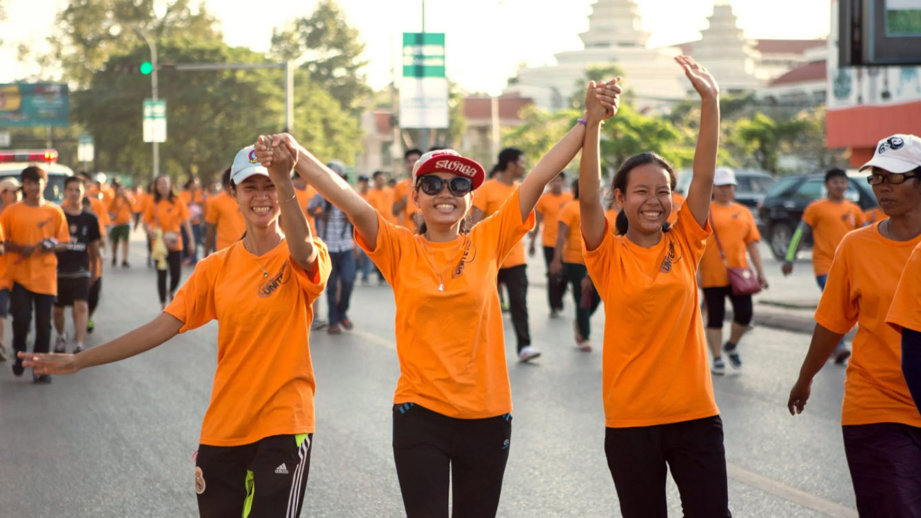 Three girls joining the Siem Reap Running Race in Cambodia in 2015. Three girls wearing orange walk among a crowd of people wearing orange.