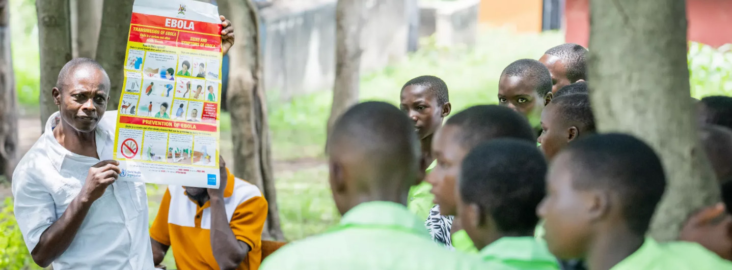 A man shows a group of children a poster explaining the steps to take to prevent the spread of the Ebola virus.